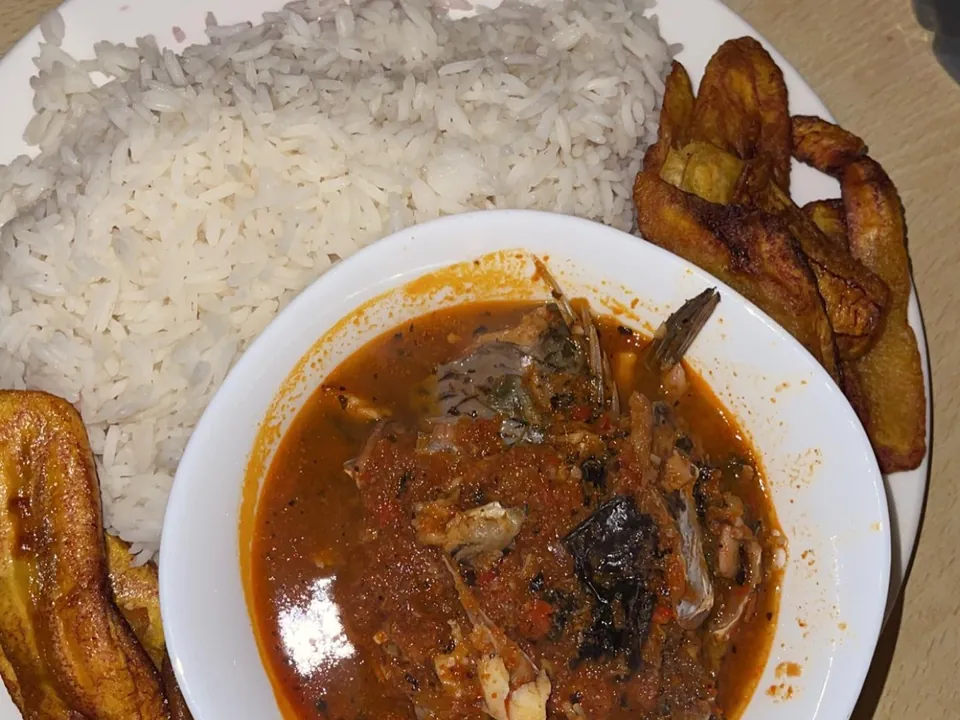 A plate of white rice with a bowl of fish soup and fried plantain