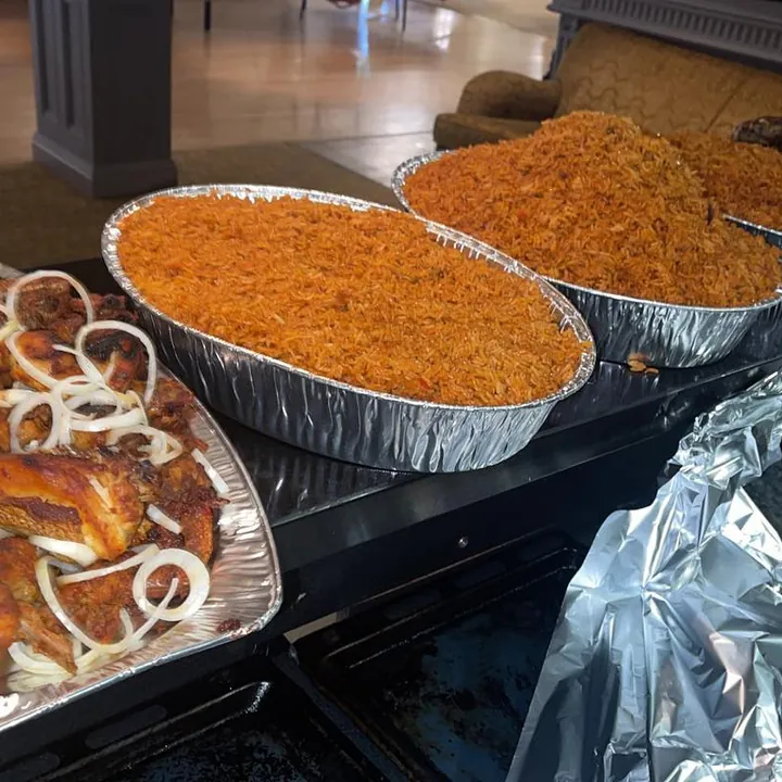 Foil trays of jollof rice and chicken laid out for a party