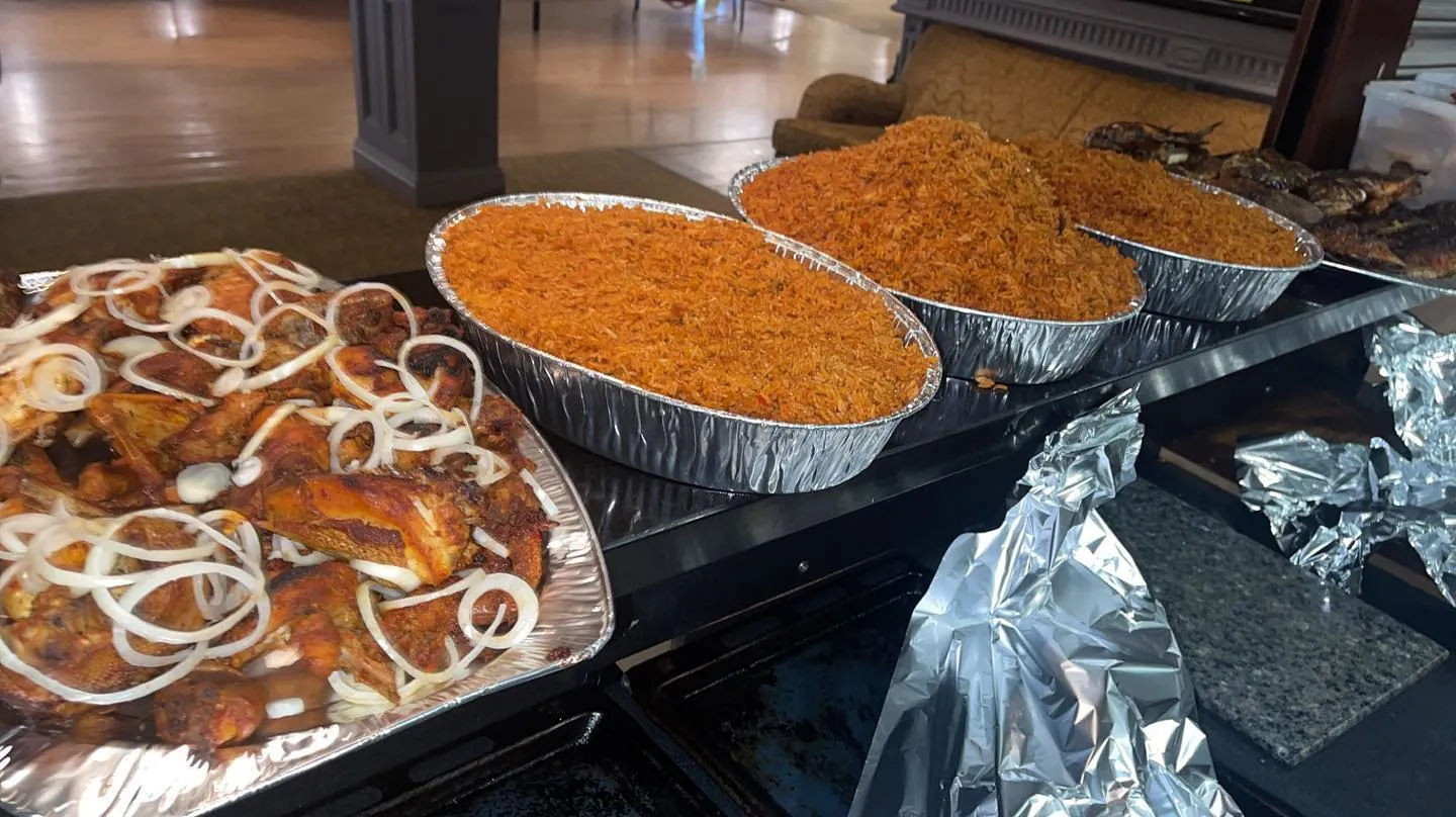 Foil trays of jollof rice and chicken laid out for a party
